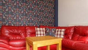 A red leather sofa with a floral-patterned wallpaper and a wooden table in front. - Blue Sparrow House (Portsmouth)