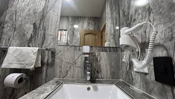 A bathroom with a marble sink, a towel rack, a mirror, a hand dryer, and a toilet paper holder.