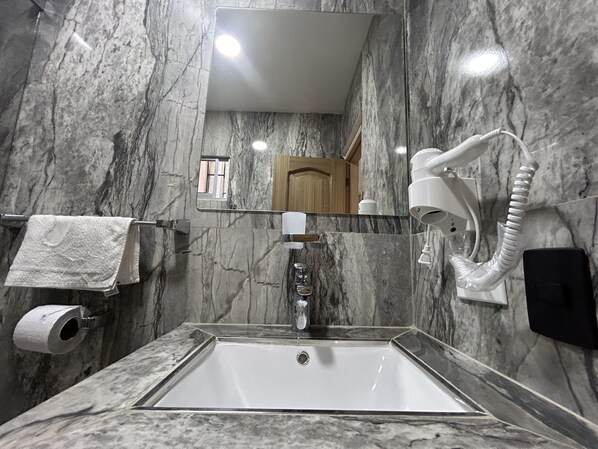 A bathroom with a marble sink, a towel rack, a mirror, a hand dryer, and a toilet paper holder. - HOTEL LA CASA 3 (Montería)