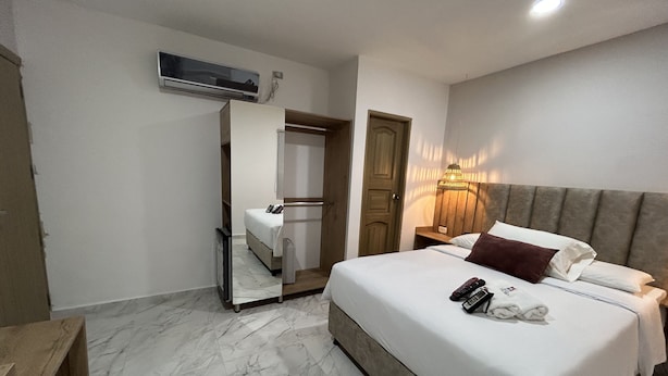 A hotel room with a large bed, a wooden headboard, a bedside table, a nightstand, a mirror, and an air conditioning unit. - HOTEL LA CASA 3 (Montería)