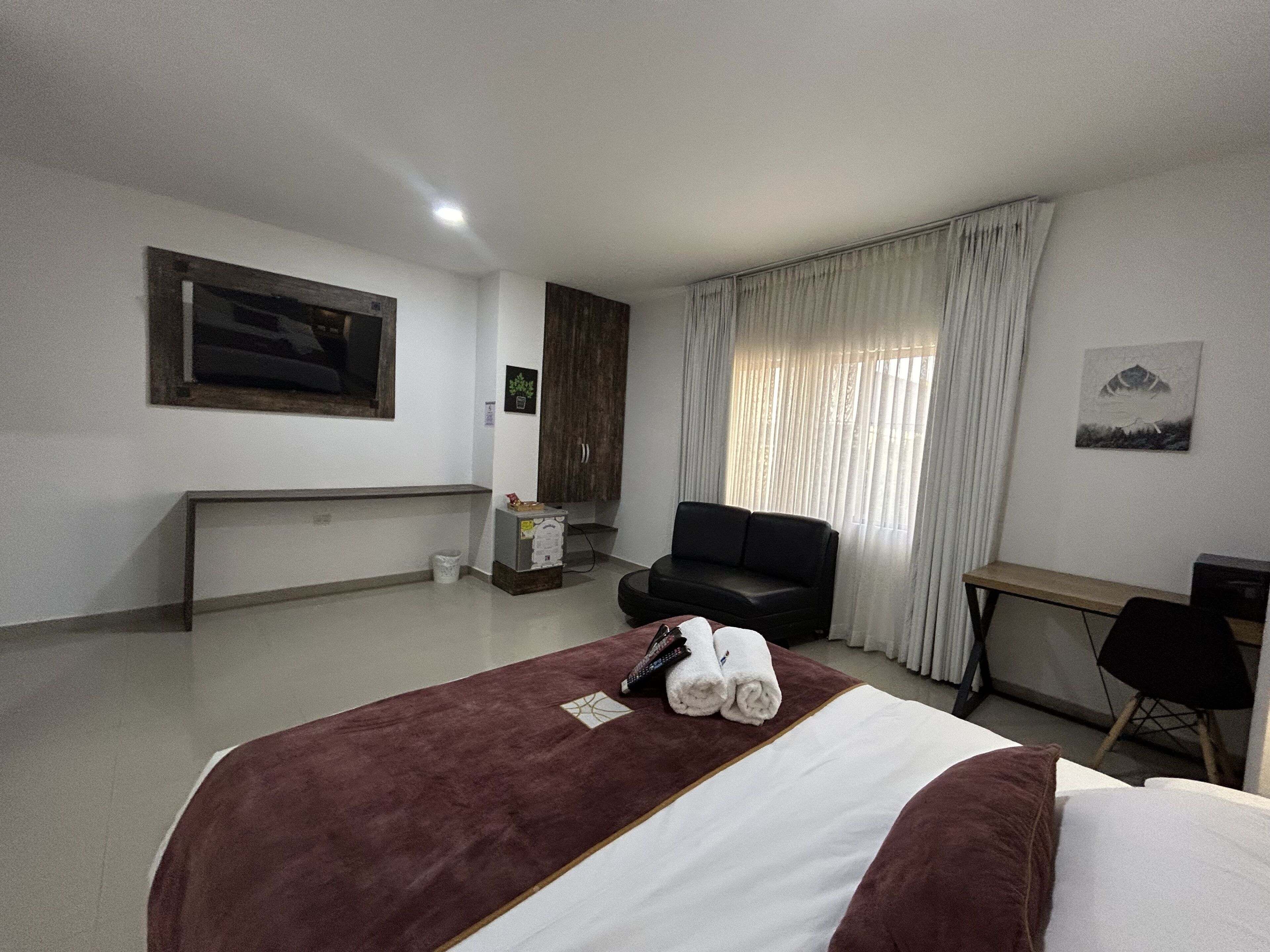 A hotel room with a bed, a desk, a chair, a wardrobe, and a window with curtains.