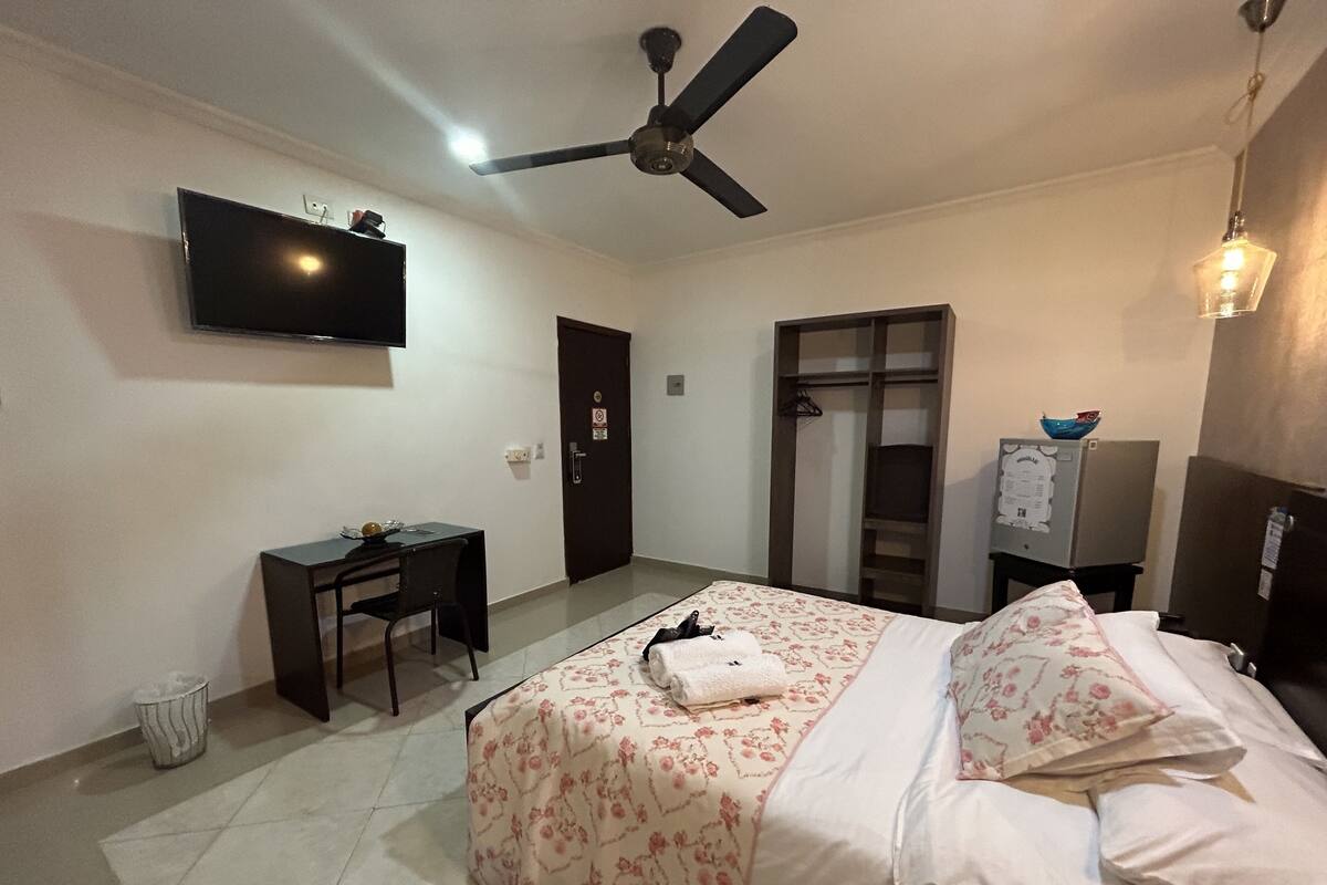 A hotel room with a bed, a desk, a television, a ceiling fan, and a wardrobe.