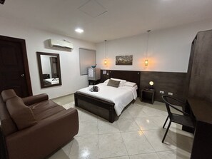 A hotel room with a bed, a sofa, a desk, a chair, a mirror, and a wall-mounted heater. - HOTEL LA CASA 3 (Montería)