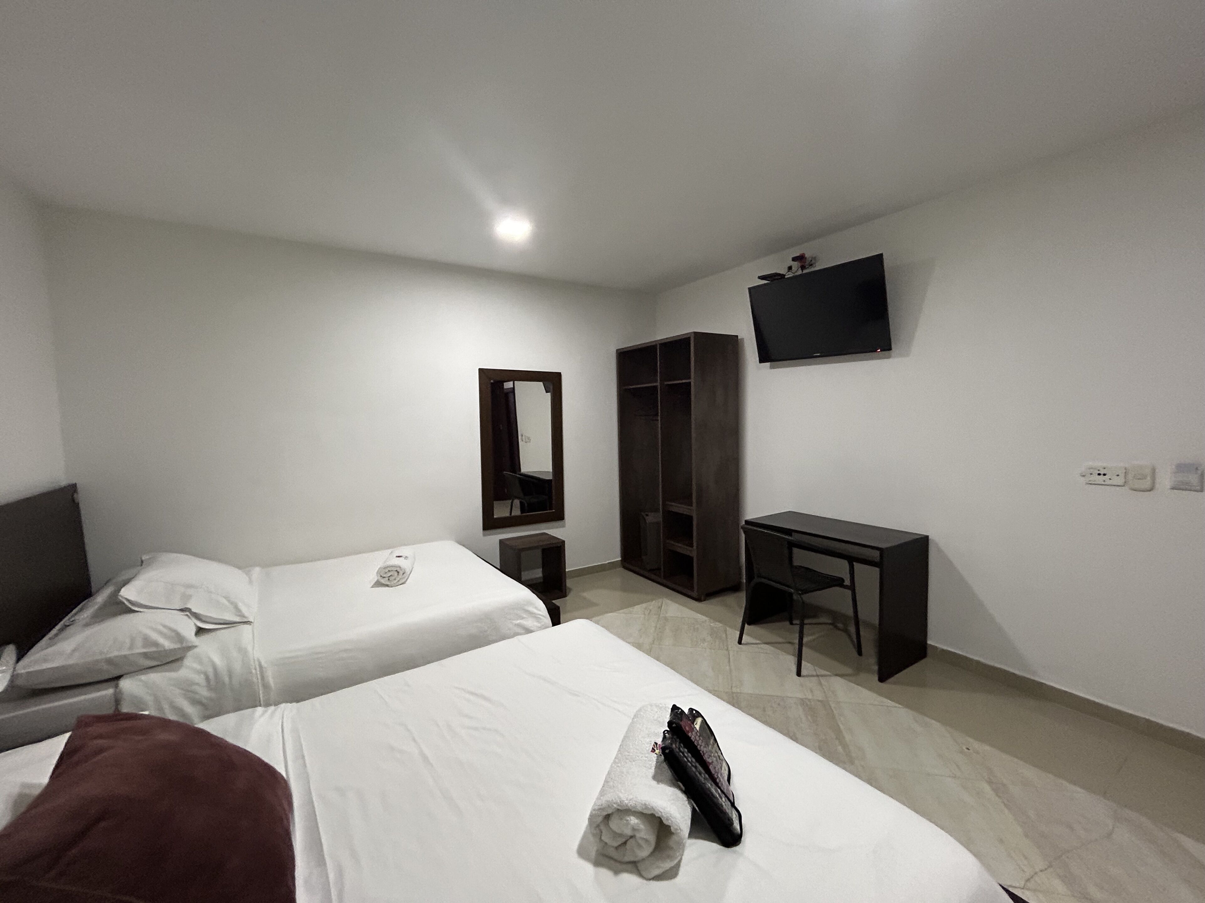 A hotel room with two beds, a desk, a wardrobe, a mirror, and a TV.