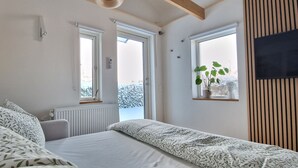 A bedroom with a bed, two windows, a radiator, and a plant on a shelf.