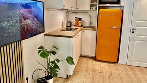 A modern kitchen with white cabinets, a wooden countertop, a built-in oven, and an orange refrigerator.