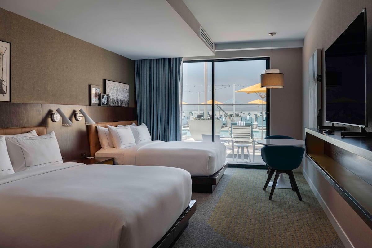 Habitación de hotel con dos camas, televisor, escritorio y vista a la ciudad.