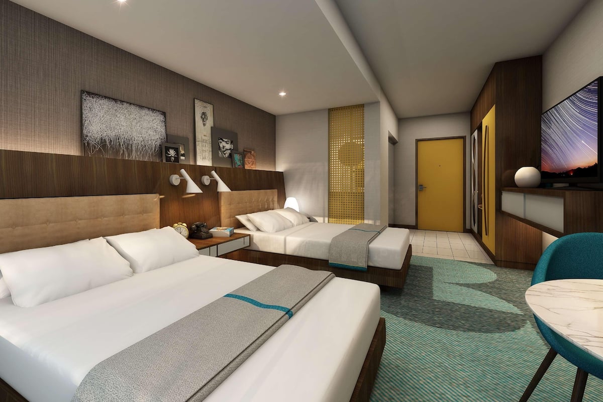 Una habitación de hotel con dos camas, un escritorio, una silla y un televisor.