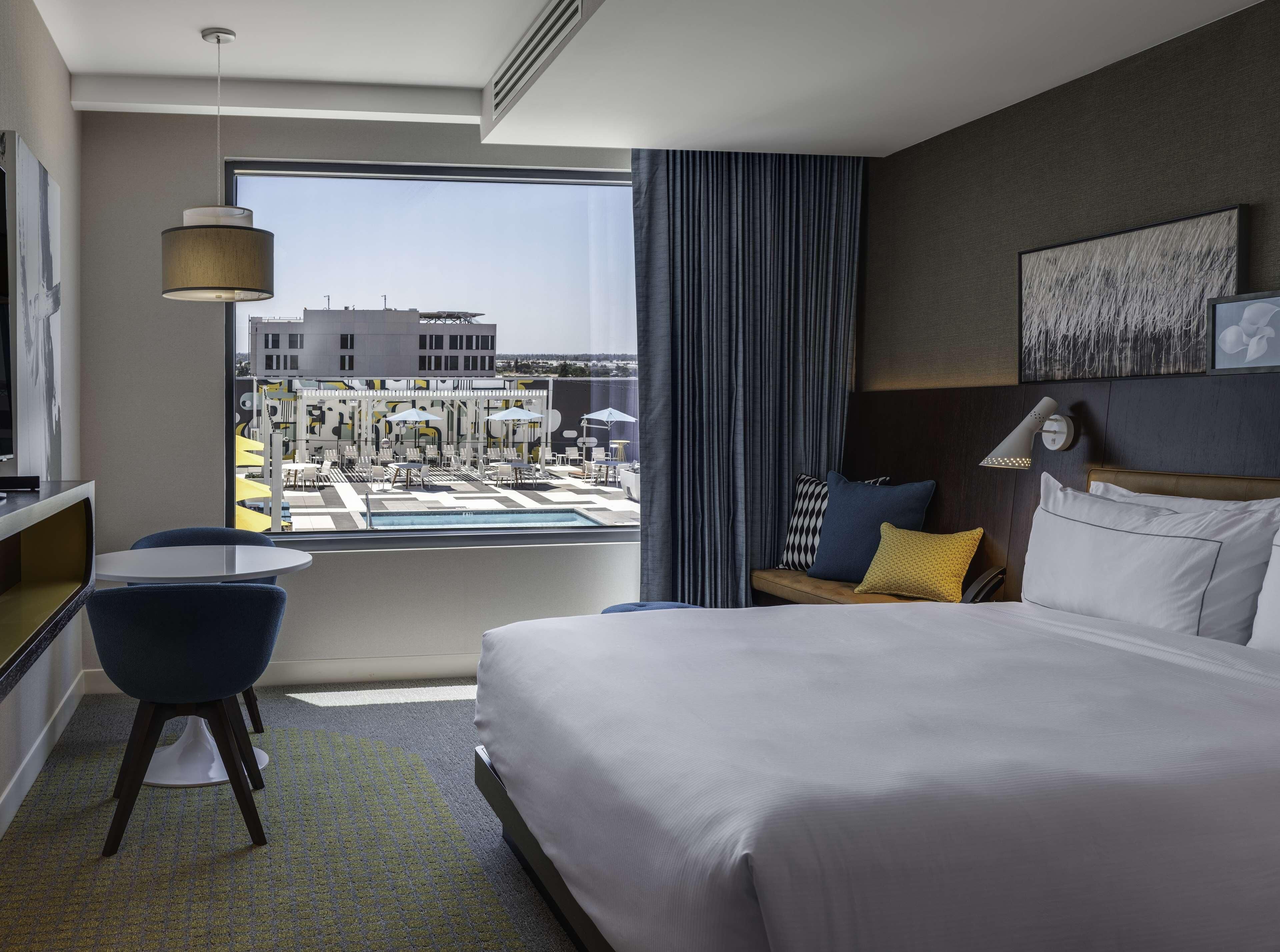 Habitación de hotel con cama, escritorio, silla, ventana con vista a un puerto deportivo y ventilador de techo.
