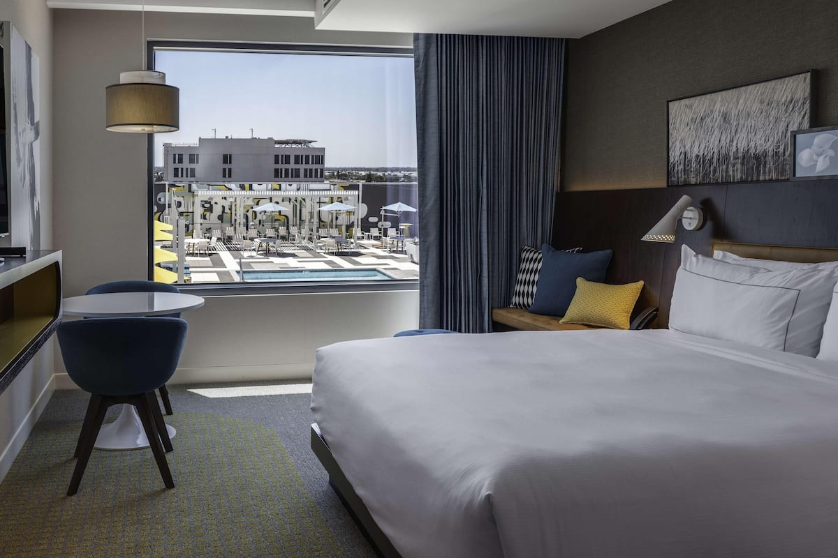 Habitación de hotel con cama, escritorio, silla, ventana con vista a un puerto deportivo y ventilador de techo.