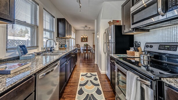 A modern kitchen with stainless steel appliances, a granite countertop, and a patterned rug. - Artist Cottage - Walk to Great Shops and Restaurants  (Oklahoma City)