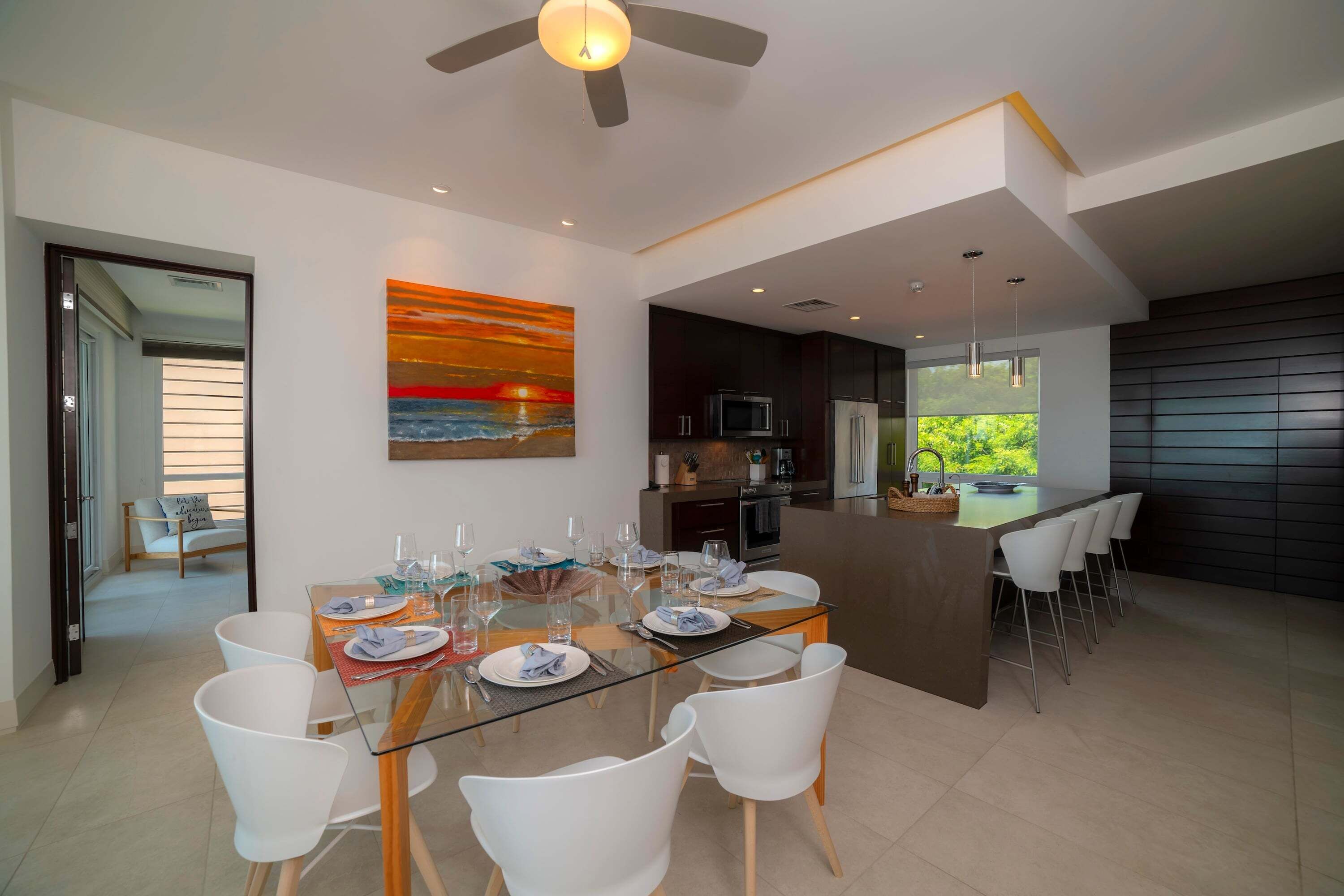 Un espace repas moderne avec une table en verre, des chaises blanches et une vue sur la cuisine.
