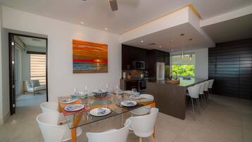 Un espace repas moderne avec une table en verre, des chaises blanches et une vue sur la cuisine.