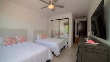 Habitación de hotel con dos camas, un ventilador de techo, un espejo grande, un televisor y una mesita con un control remoto.