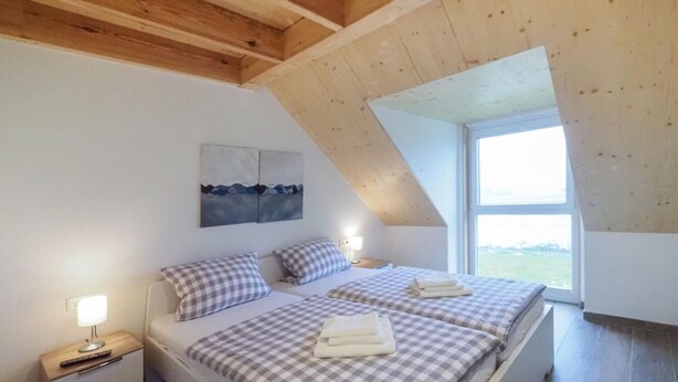 A bedroom with two beds, a nightstand, a lamp, a painting, and a large window. - Ferienpark Wolfsschlucht (Prüm/OT Walcherath)