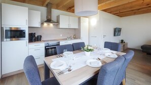 A modern kitchen with white cabinets, stainless steel appliances, and a dining area with a wooden table set for six. - Ferienpark Wolfsschlucht (Prüm/OT Walcherath)