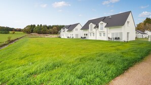 A row of white houses with dark roofs, set in a green field with a clear sky. - Ferienpark Wolfsschlucht (Prüm/OT Walcherath)