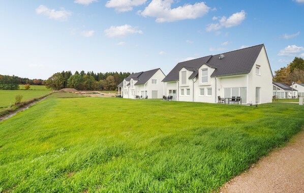 A row of white houses with dark roofs, set in a green field with a clear sky.