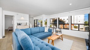 A modern living room with a sectional sofa, a wooden coffee table, and large windows offering views of the city.