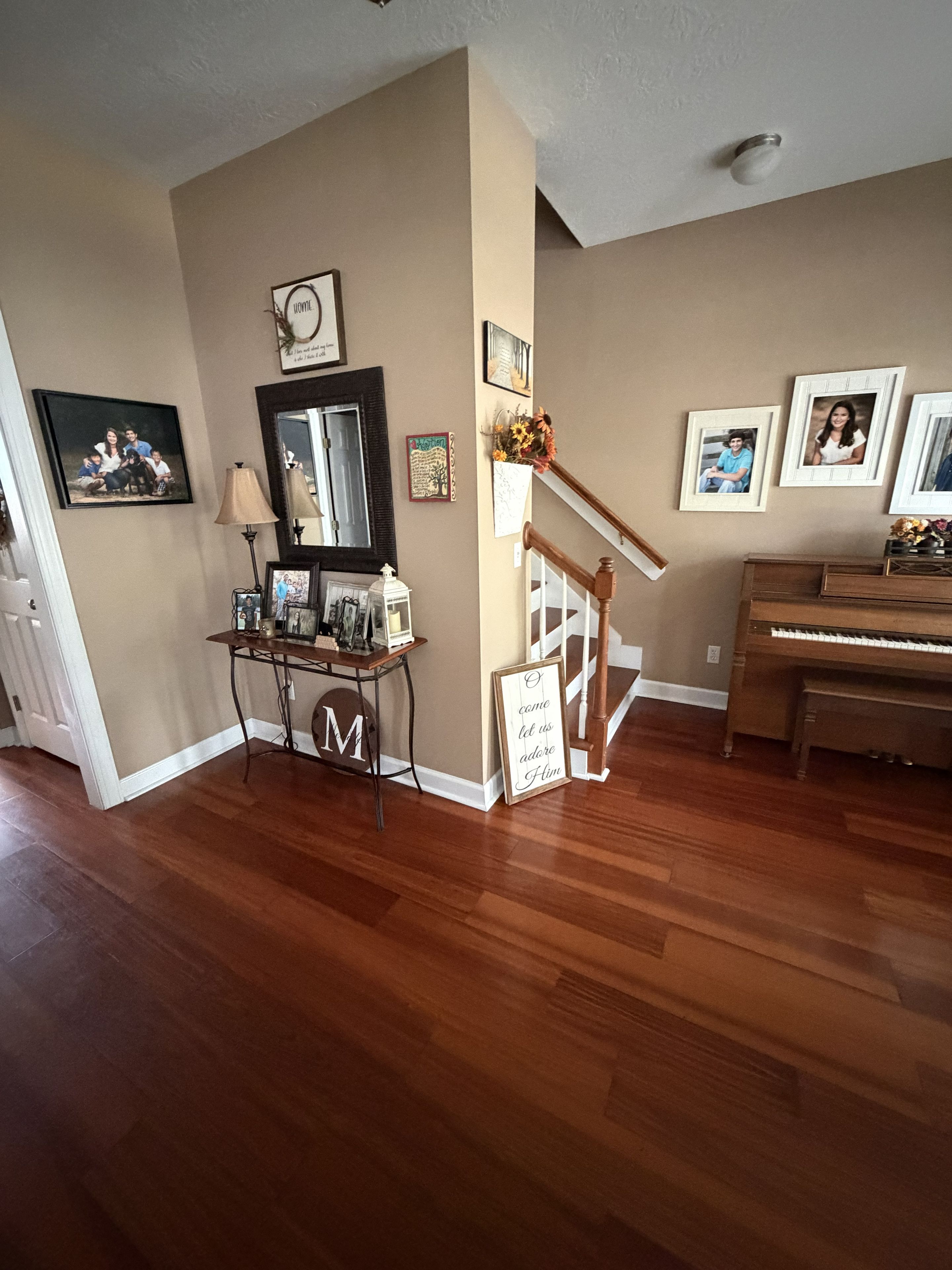 Una sala de estar con piso de madera, un piano, una escalera y varias fotografías enmarcadas en las paredes.