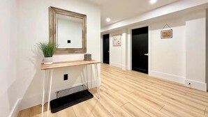 A hallway with wooden flooring, a white console table with a potted plant, a mirror, and black doors. - Modern, Bright, Spacious 2 Bedroom Guest Suite - Entire Separate Basement  (Grimsby)
