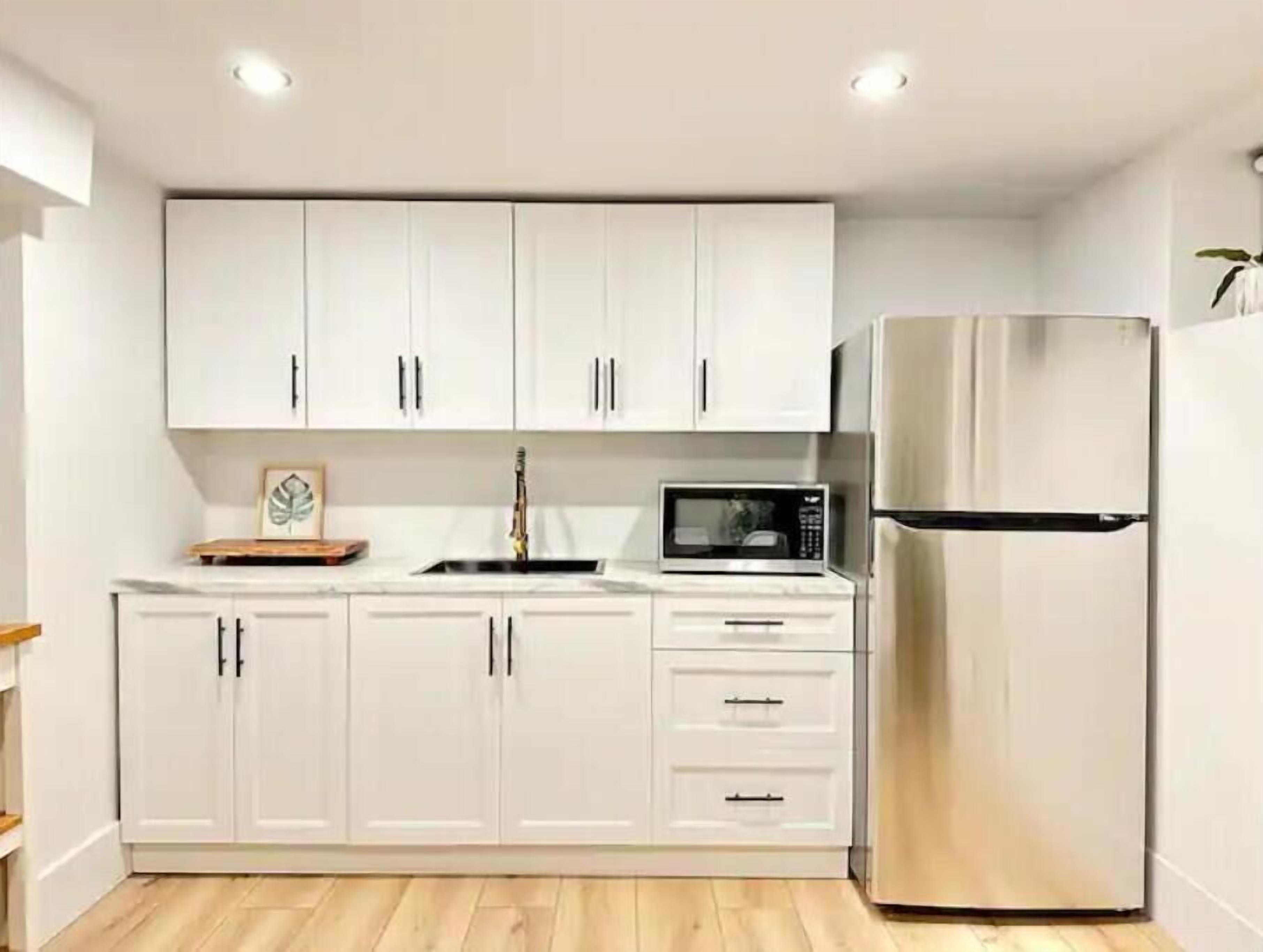 A modern kitchen with white cabinets, a stainless steel refrigerator, and a microwave.