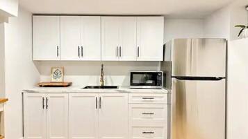 A modern kitchen with white cabinets, a stainless steel refrigerator, and a microwave.