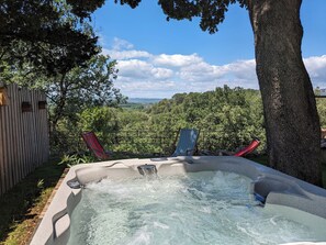 Een hottub met waterval, omringd door een houten hek en bomen, met uitzicht op een weelderig landschap.