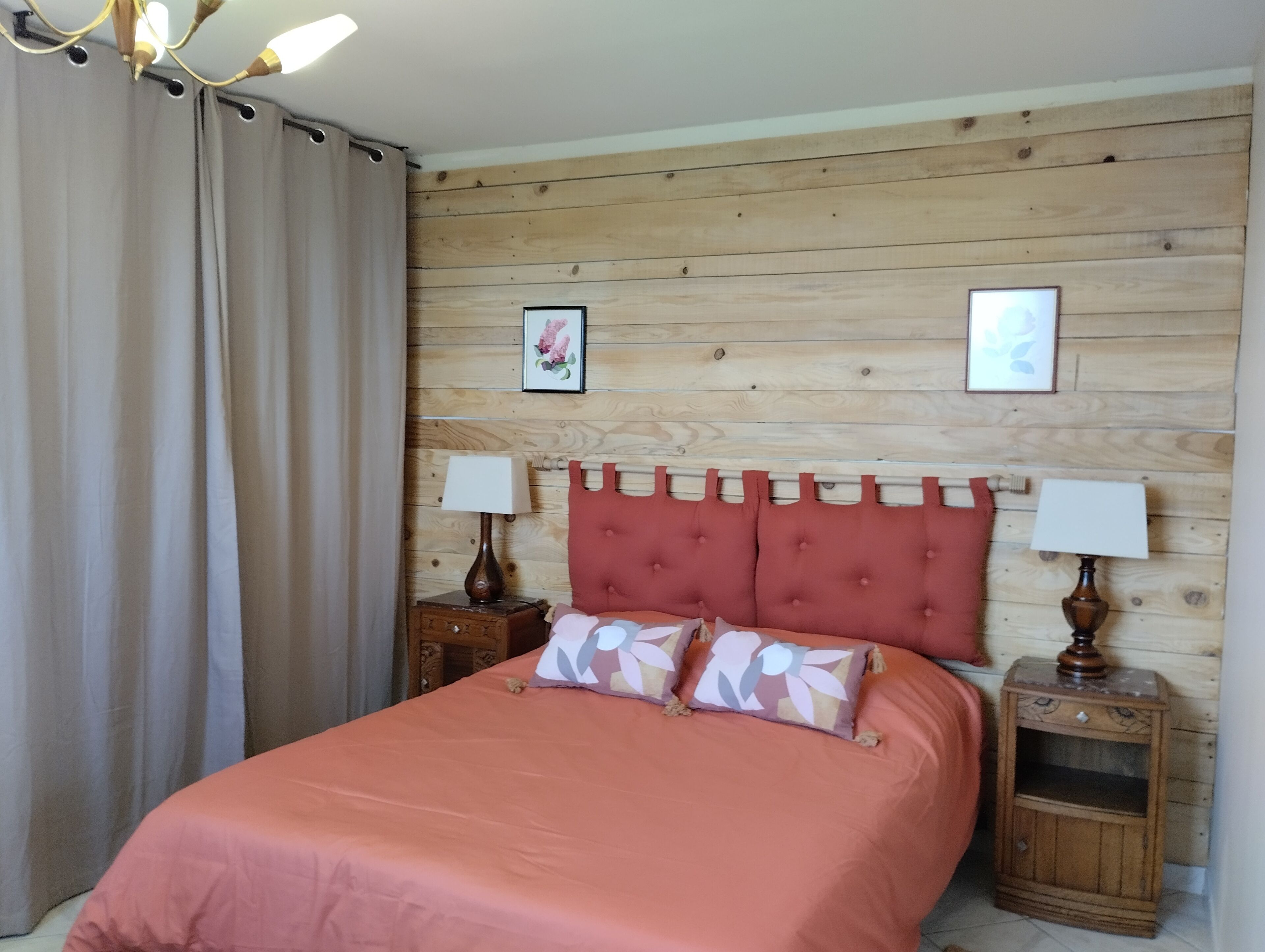 A bedroom with a wooden headboard, a pink bedspread, two bedside tables with lamps, and a window with curtains.