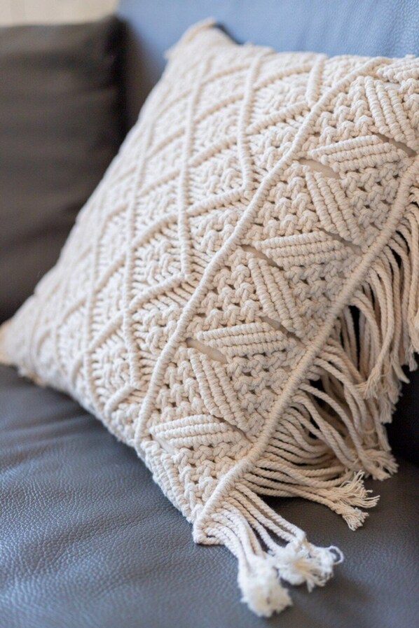 A macramé throw blanket with fringe details on a grey sofa.