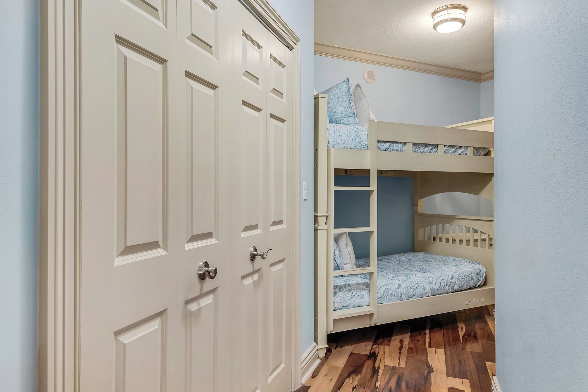 A room with a bunk bed, a white door, and a wooden floor.