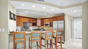 Una cocina moderna con armarios de madera, un refrigerador de acero inoxidable, un microondas y una barra con cuatro taburetes.