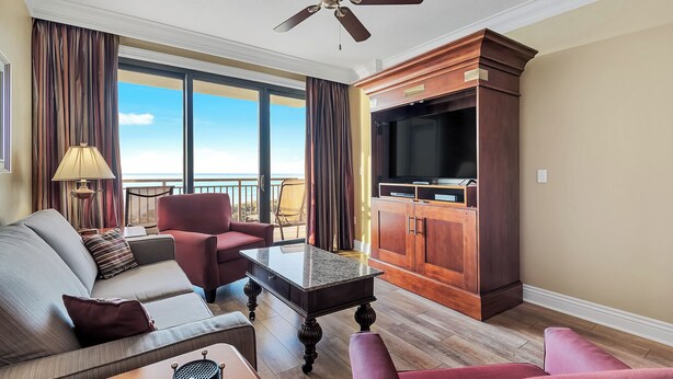 Habitación de hotel con sofá, sillones, una mesa de centro, televisor y un mueble de madera.