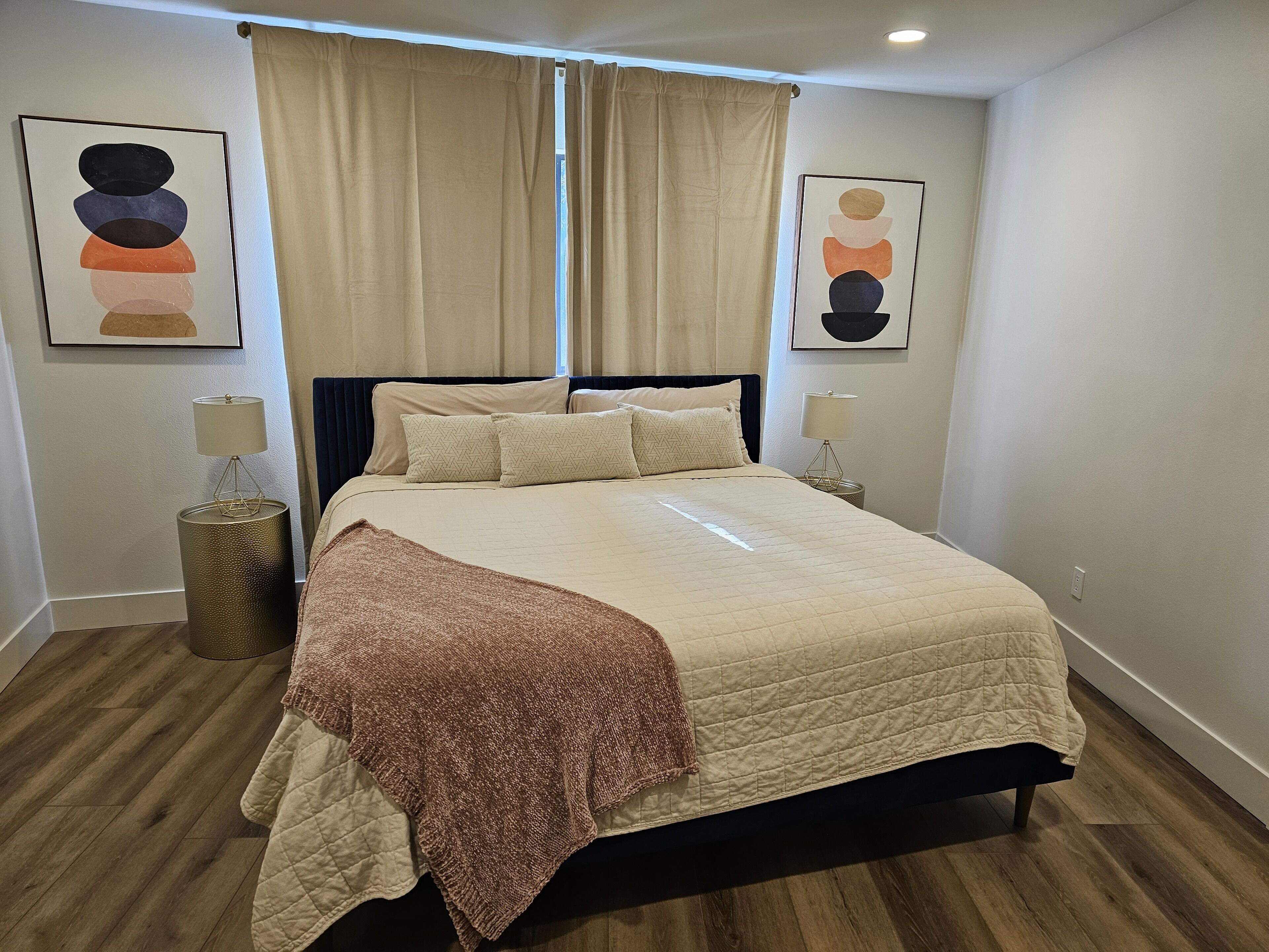 A neatly made bed with a quilted cover, two bedside lamps, and a decorative lamp on a round base.