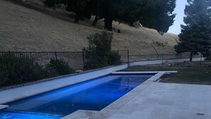 En swimmingpool med ett kaklat poolområde, en flätad loungestol och ett staket.