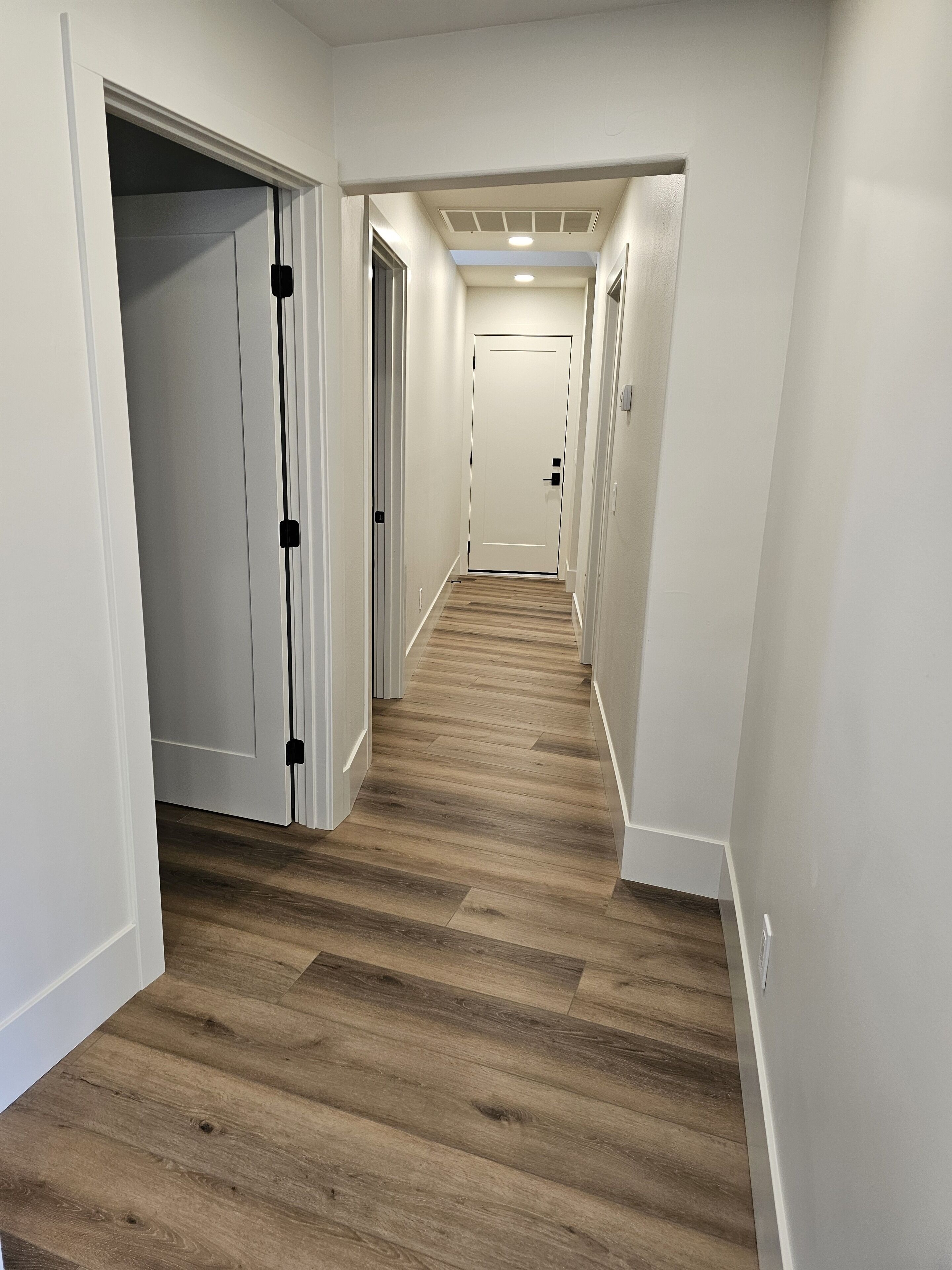 Un pasillo estrecho con suelo de madera y paredes blancas, que conduce a una puerta cerrada al final.
