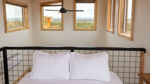 A bedroom with a bed, a ceiling fan, and three windows with a view of the landscape. - Tiny Cabin, #1 Lamb Point View @ The Cedars (Kanab)