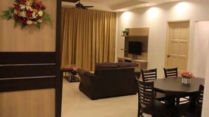 A living room with a sofa, a dining table with chairs, a TV mounted on the wall, and a ceiling fan. - Crown Imperial Court Apartment Brinchang #3 (Cameron Highlands)