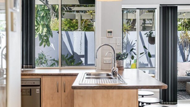 A modern kitchen with a large window, a sink, and a dining area with a table and chairs.