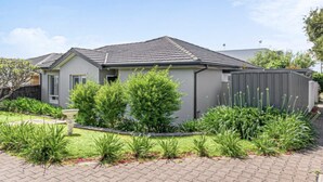 A modern two-story house with a grey exterior, a tiled roof, and a well-maintained garden with various plants and a small tree.