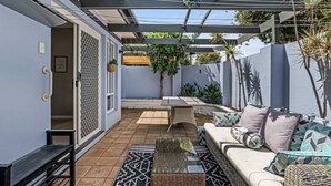 A covered patio area with a sofa, cushions, a small table, and a bench.