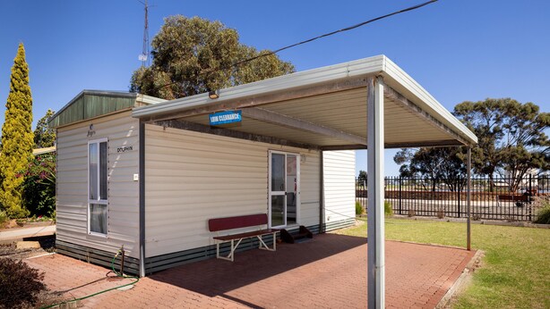 A small, single-story building with a covered porch, a bench, and a sign indicating 'LOW GUARDANCE.' - Echo Holiday Parks - Port Pirie (Solomontown)