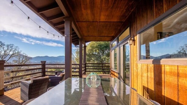 A covered outdoor area with a glass table, wicker chairs, and a view of mountains. - Verona: Awesome Views, Pool, Vineyard, Hot Tub! (Ukiah)