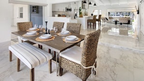 A modern dining area with a marble floor, woven chairs, and a central island with kitchen appliances. - Lux FL Waterfront Heaven, Pool, Jacuzzi, World Cup? Stadium is Only 15 Mins Away (Fort Lauderdale)