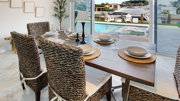 A dining area with wicker chairs, a wooden table, and a view of a pool and boats outside. - Lux FL Waterfront Heaven, Pool, Jacuzzi, World Cup? Stadium is Only 15 Mins Away (Fort Lauderdale)