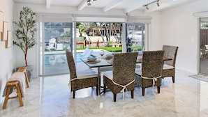 A modern dining area with a glass door leading to a poolside view, wicker chairs, a marble floor, and a bench. - Lux FL Waterfront Heaven, Pool, Jacuzzi, World Cup? Stadium is Only 15 Mins Away (Fort Lauderdale)