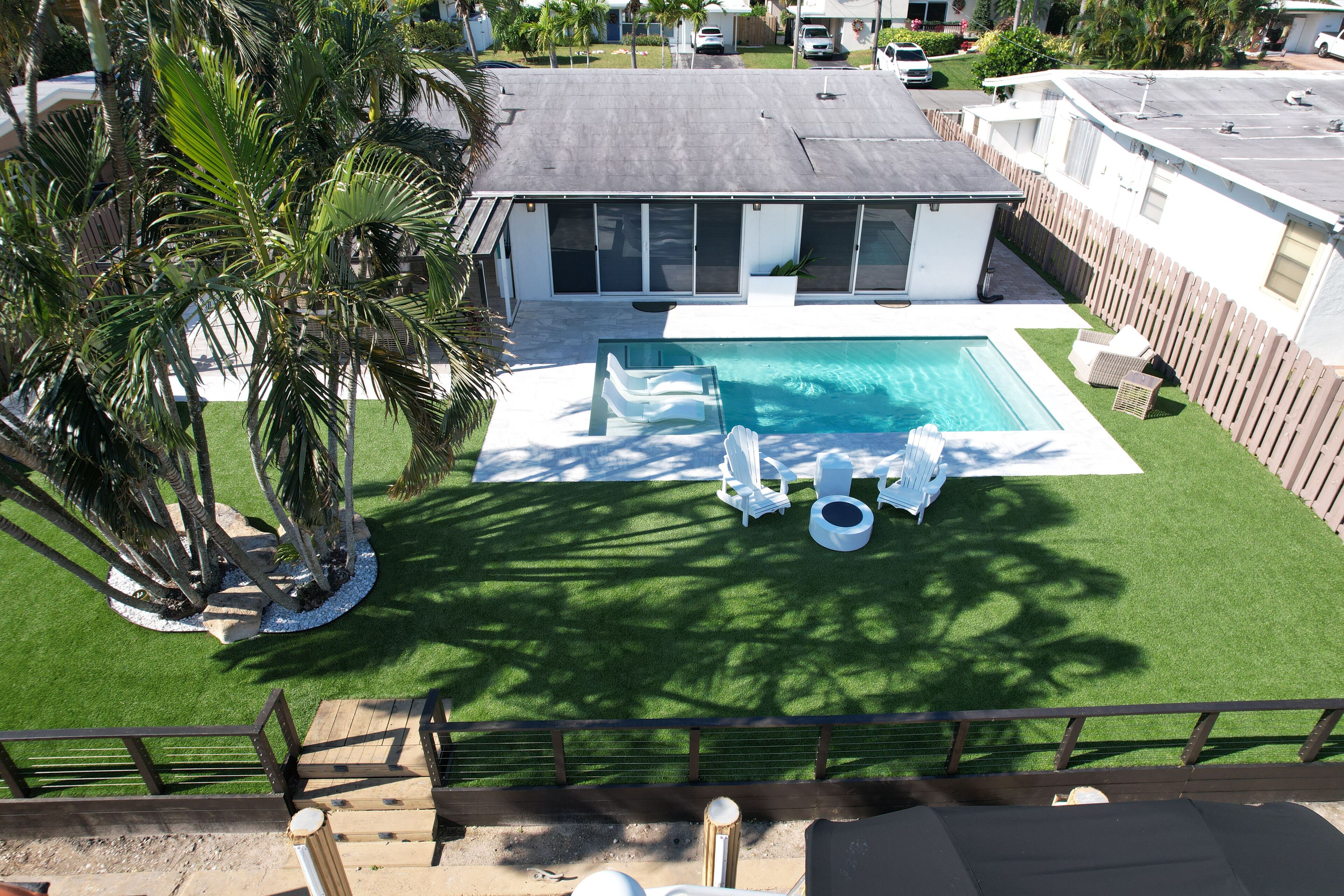 A modern house with a swimming pool, surrounded by a wooden fence and palm trees.