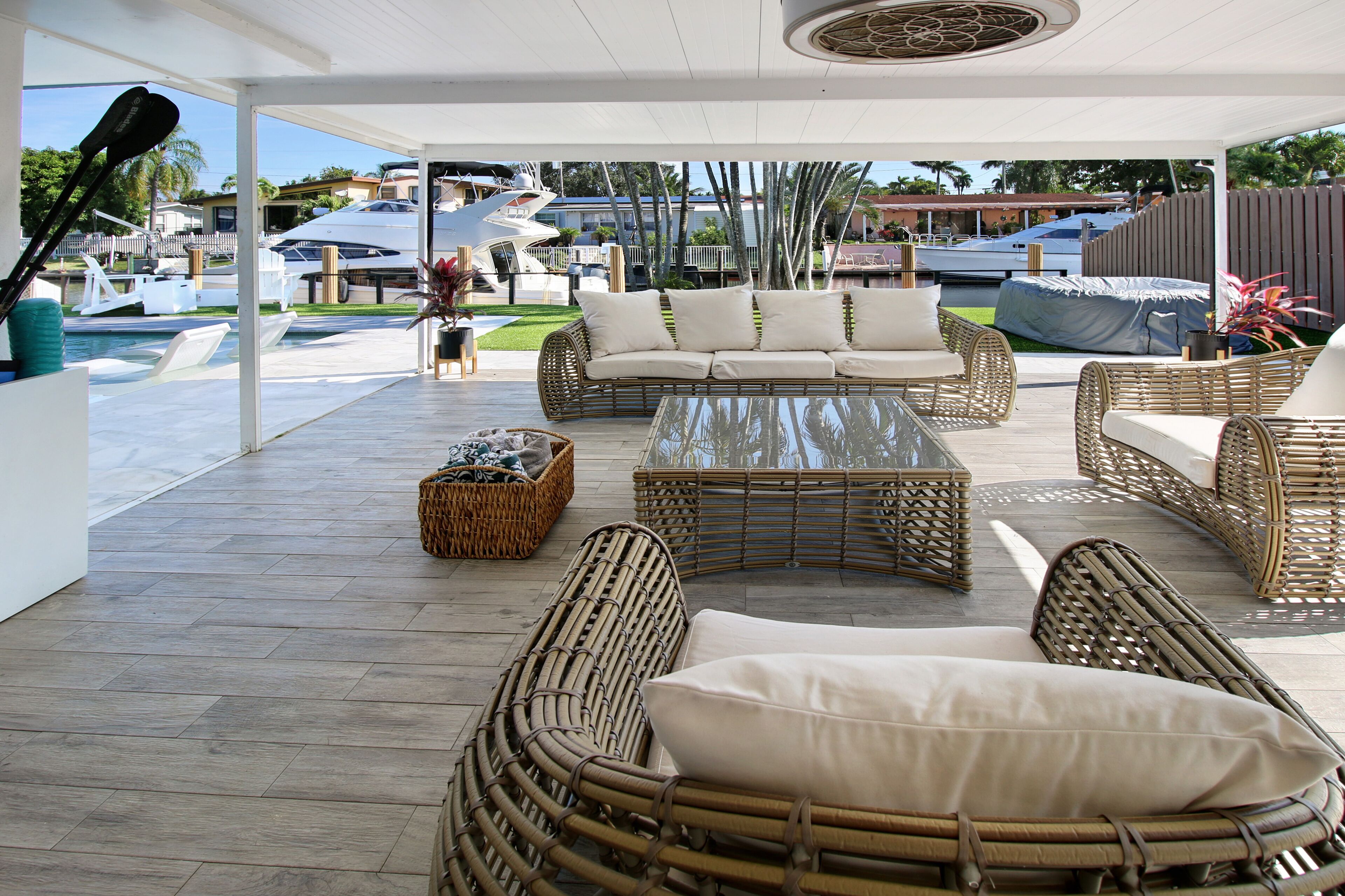 Un espace extérieur aménagé, abrité et doté de mobilier en osier, d’une table en verre et offrant une vue sur les yachts et la piscine.