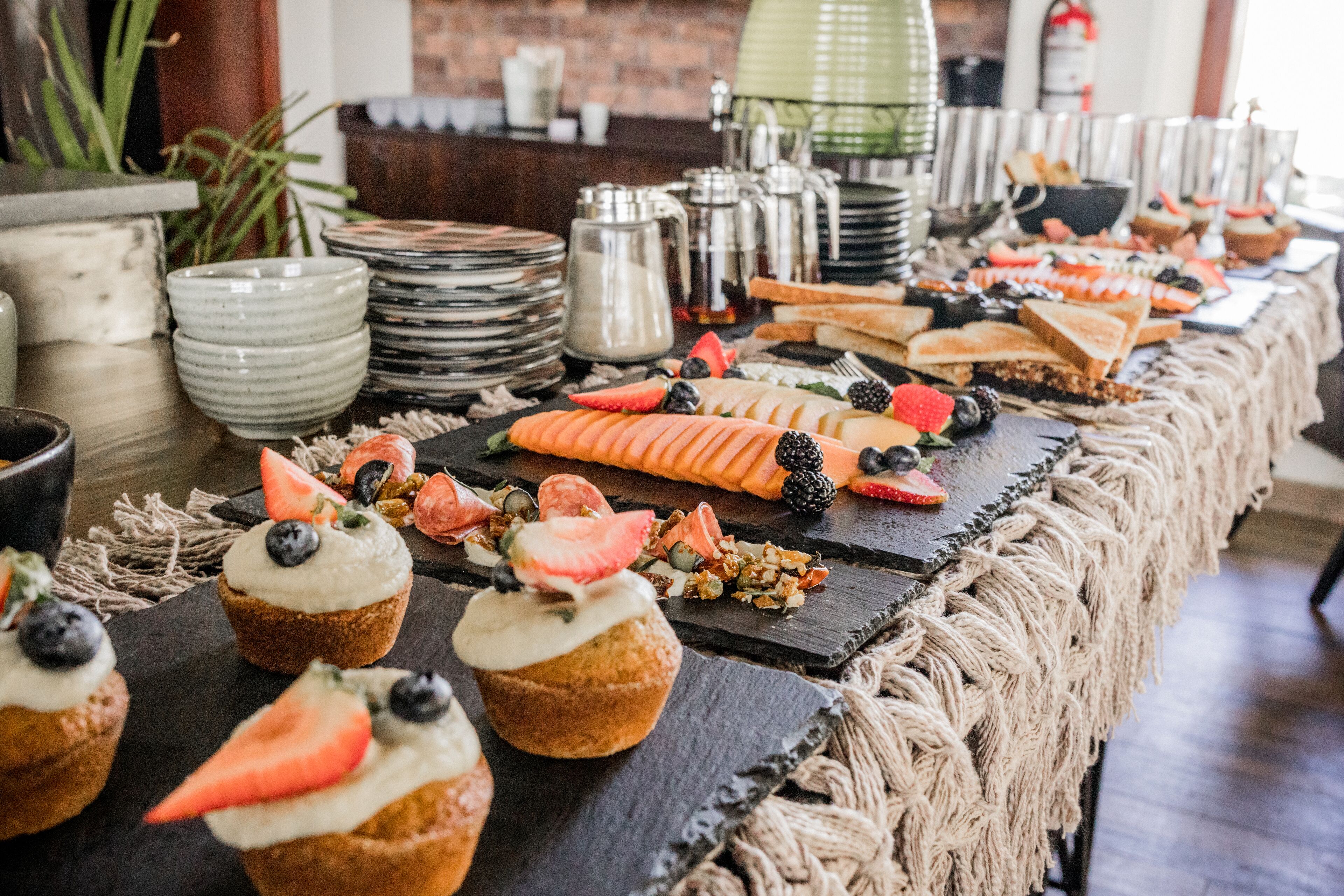 A buffet table with various food items, including cupcakes with fruit toppings, sandwiches, and a spread of vegetables.