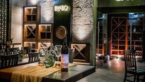 A restaurant interior with a wooden table, wine glasses, and a bottle of wine. There is a wall with a clock and a sign that reads "CAVA". - Limbo Hotel Boutique (Valle de Guadalupe)